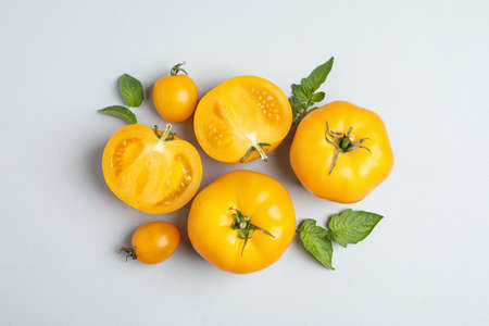 Cut and whole ripe yellow tomatoes with leaves on light background, flat layの写真素材