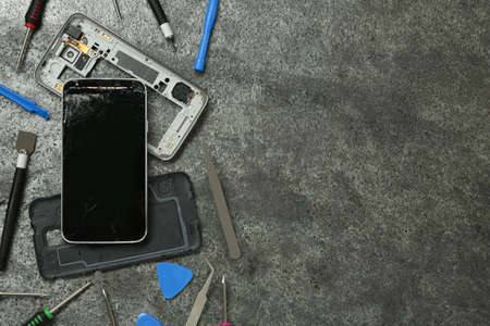 Parts of damaged smartphone and repair tool set on gray table, flat lay. Space for text