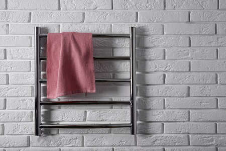 Modern heated towel rail with warm soft towel on white brick wall. Space for textの写真素材