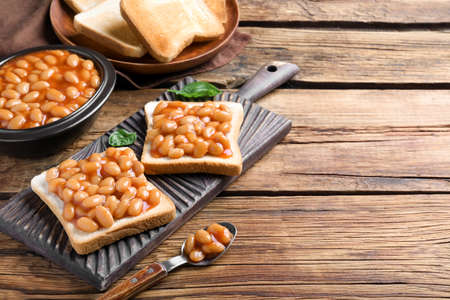Toasts with delicious canned beans on wooden table, space for text