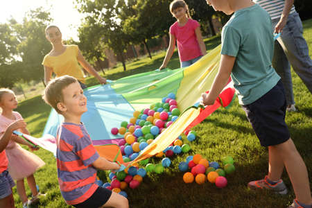 Group of children and teacher playing with rainbow playground parachute on green grass. Summer camp activityの写真素材