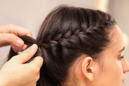 Professional stylist braiding client's hair on blurred background, closeup