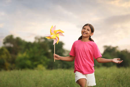 Cute little girl with pinwheel in field, space for text. Child spending time in natureの写真素材