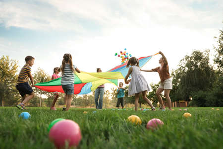 Group of children and teachers playing with rainbow playground parachute on green grass, low angle view. Summer camp activityの写真素材