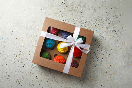 Box with delicious colorful cupcakes and confetti on light gray table, flat lay