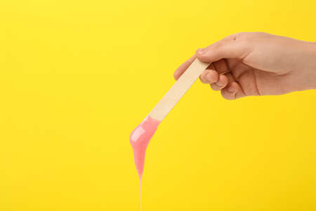 Woman holding spatula with hot depilatory wax on yellow background, closeupの写真素材
