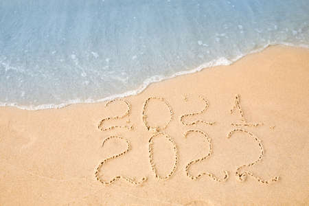Dates written on sandy beach. 2021 washed by sea wave as New 2022 Year coming, above view