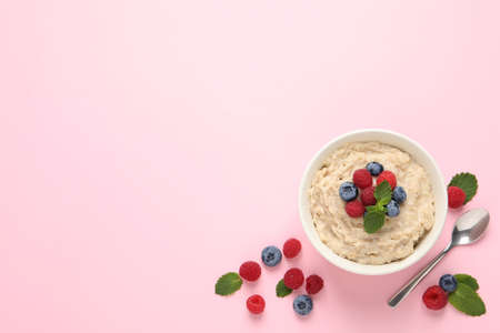 Tasty oatmeal porridge with raspberries and blueberries in bowl on pink background, flat lay. Space for textの写真素材