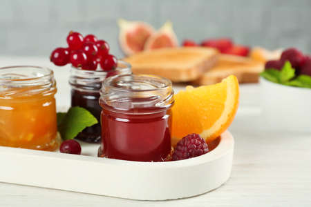 Jars with different sweet jams and ingredients on white wooden table