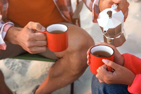 Couple enjoying hot drink outdoors, closeup. Beach campingの写真素材