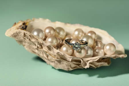 Beautiful engagement ring with gemstone and pearls in shell on mint backgroundの写真素材