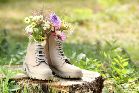 Beautiful flowers in boots on stump outdoors, space for textの写真素材
