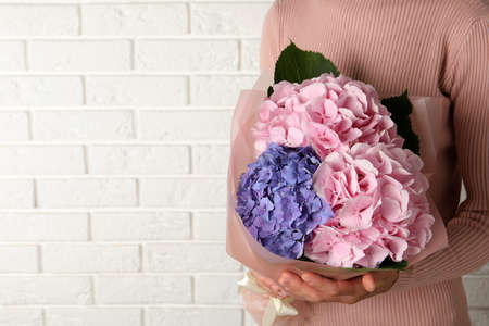 Woman with bouquet of beautiful hortensia flowers near white brick wall, closeup. Space for textの写真素材