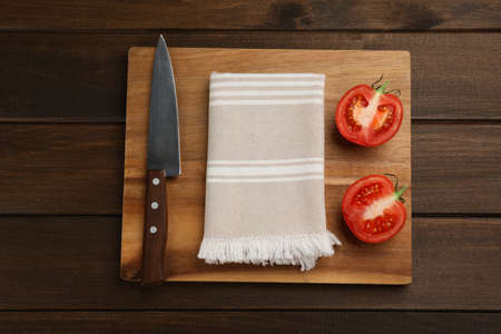 Cutting board with kitchen towel, halved tomato and knife on wooden table, top viewの写真素材