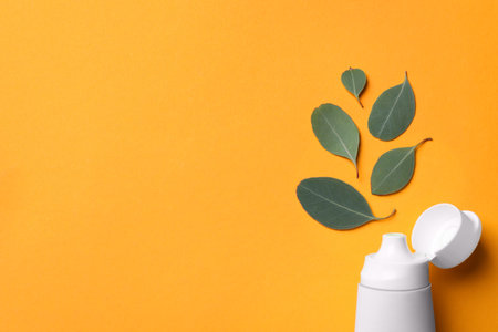 Blank tube of toothpaste and eucalyptus leaves on orange background, flat lay. Space for text
