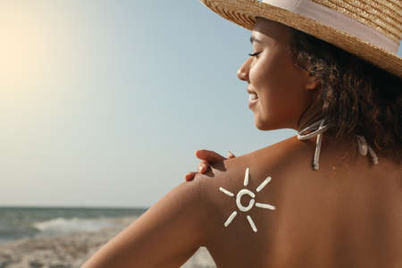 Beautiful African American woman with sun protection cream on shoulder at beachの写真素材