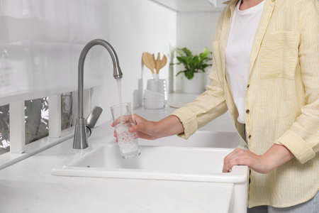Woman filling glass with water from tap in kitchen, closeupの写真素材