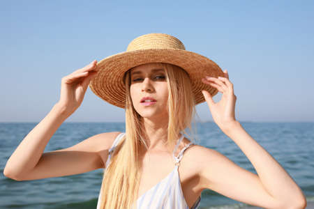 Beautiful young woman with straw hat near sea on sunny day in summerの写真素材