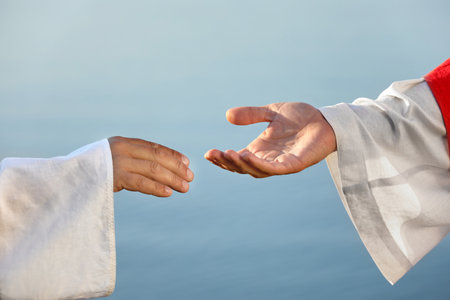 Man reaching for Jesus Christ's hand near water outdoors, closeupの写真素材