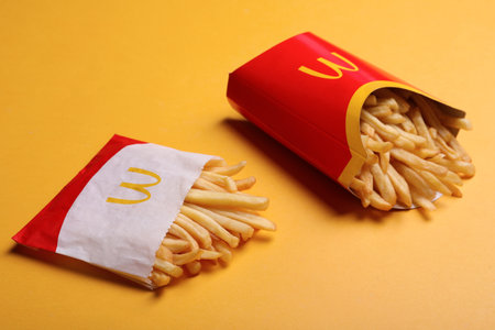 MYKOLAIV, UKRAINE - AUGUST 12, 2021: Small and big portions of McDonald's French fries on orange...