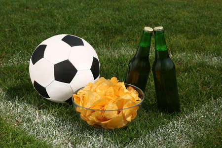 Football ball with beer and chips on green field grassの写真素材