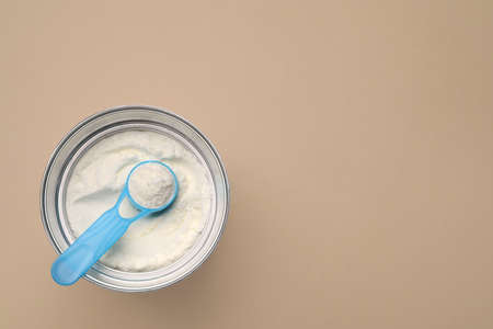 Top view of powdered infant formula with scoop in can on beige background, space for text. Baby milk