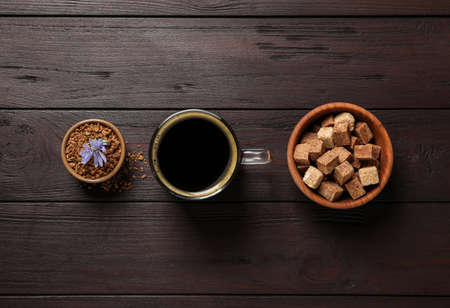 Glass cup of delicious chicory drink, granules, brown sugar and flower on wooden table, flat layの写真素材