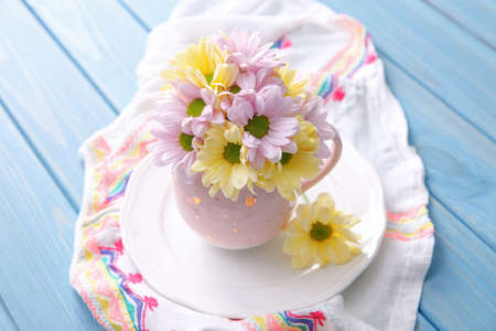 Bouquet of beautiful flowers in cup on light blue wooden table