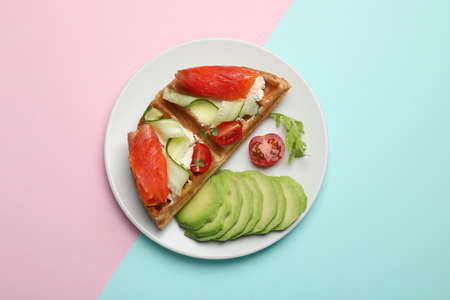 Delicious Belgian waffle with salmon, avocado, cream cheese and vegetables on color background, top viewの写真素材