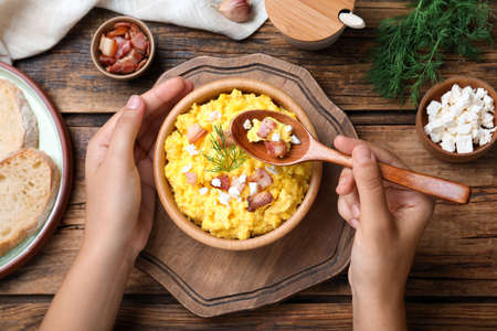 Woman eating banosh with brynza and pork cracklings at wooden table, top view. Traditional Ukrainian dishの写真素材