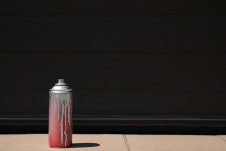 Used can of spray paint on tile floor near black wall outdoors, space for text. Graffiti suppliesの写真素材