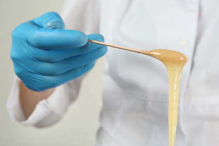Woman in gloves holding spatula with hot depilatory wax, closeupの写真素材