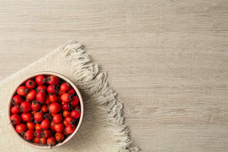 Ripe rose hip berries in bowl on wooden table, top view. Space for textの写真素材