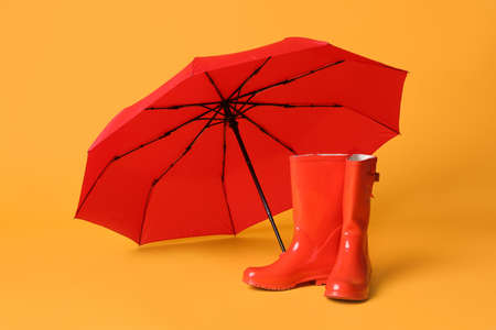 Open red umbrella and rubber boots on yellow backgroundの写真素材
