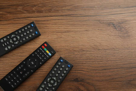 Modern tv remote controls on wooden table, flat lay. Space for textの写真素材