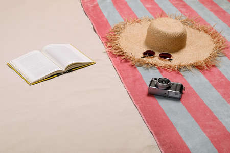 Beach towel, hat, sunglasses, camera and open book on sandの写真素材