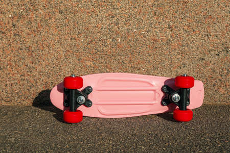 Pink skateboard with red wheels on asphalt outdoors