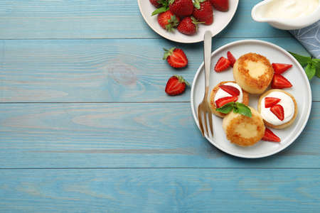 Delicious cottage cheese pancakes with strawberries, honey and sour cream on light blue wooden table, flat lay. Space for textの写真素材