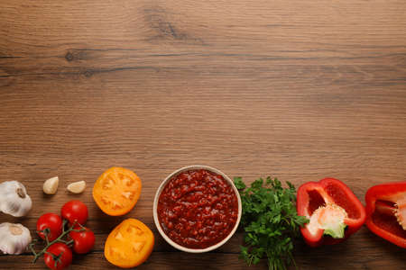 Delicious adjika sauce in bowl and ingredients on wooden table, flat lay. Space for textの写真素材