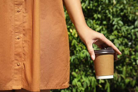 Woman holding takeaway cardboard coffee cup with plastic lid outdoors, closeupの写真素材