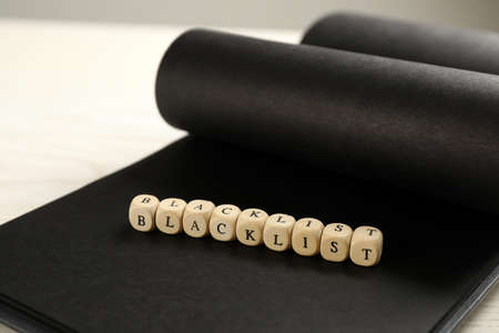 Wooden cubes with word Blacklist and notebook on table, closeupの写真素材