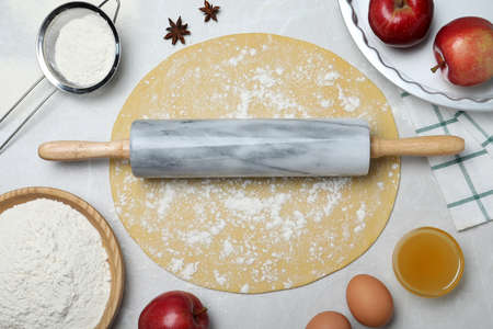 Flat lay composition with raw dough and ingredients on light gray table. Baking apple pie