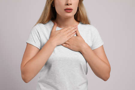 Young woman suffering from pain during breathing on light gray background, closeup