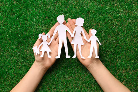 Woman holding family paper cutout on green grass, top viewの写真素材