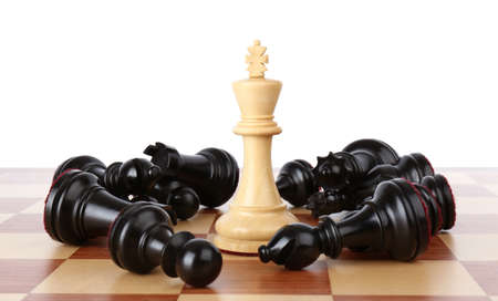 King among fallen black chess pieces on wooden board against white background