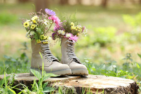 Beautiful flowers in boots on stump outdoors, space for text