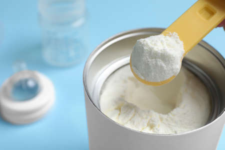 Scoop of powdered infant formula over can on light blue background, closeup. Baby milkの写真素材