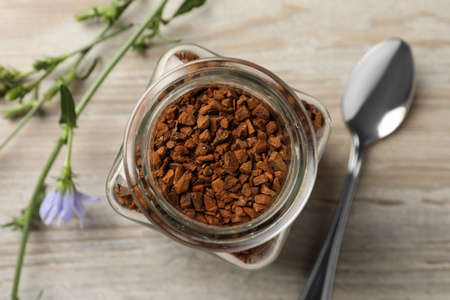 Jar of chicory granules on white wooden table, top view