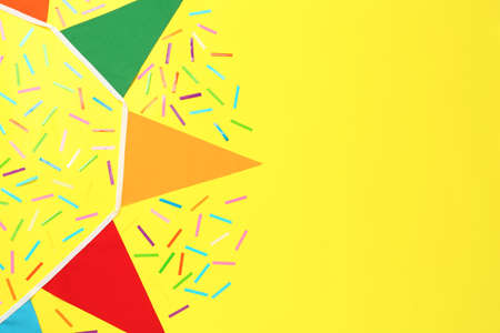 Bunting with colorful triangular flags and confetti on yellow background, flat lay. Space for text