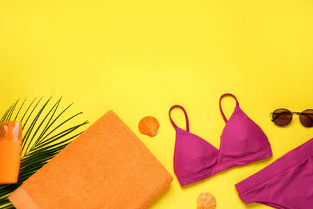 Beach towel, swimsuit, sunglasses and sun protection product on yellow background, flat lay. Space...